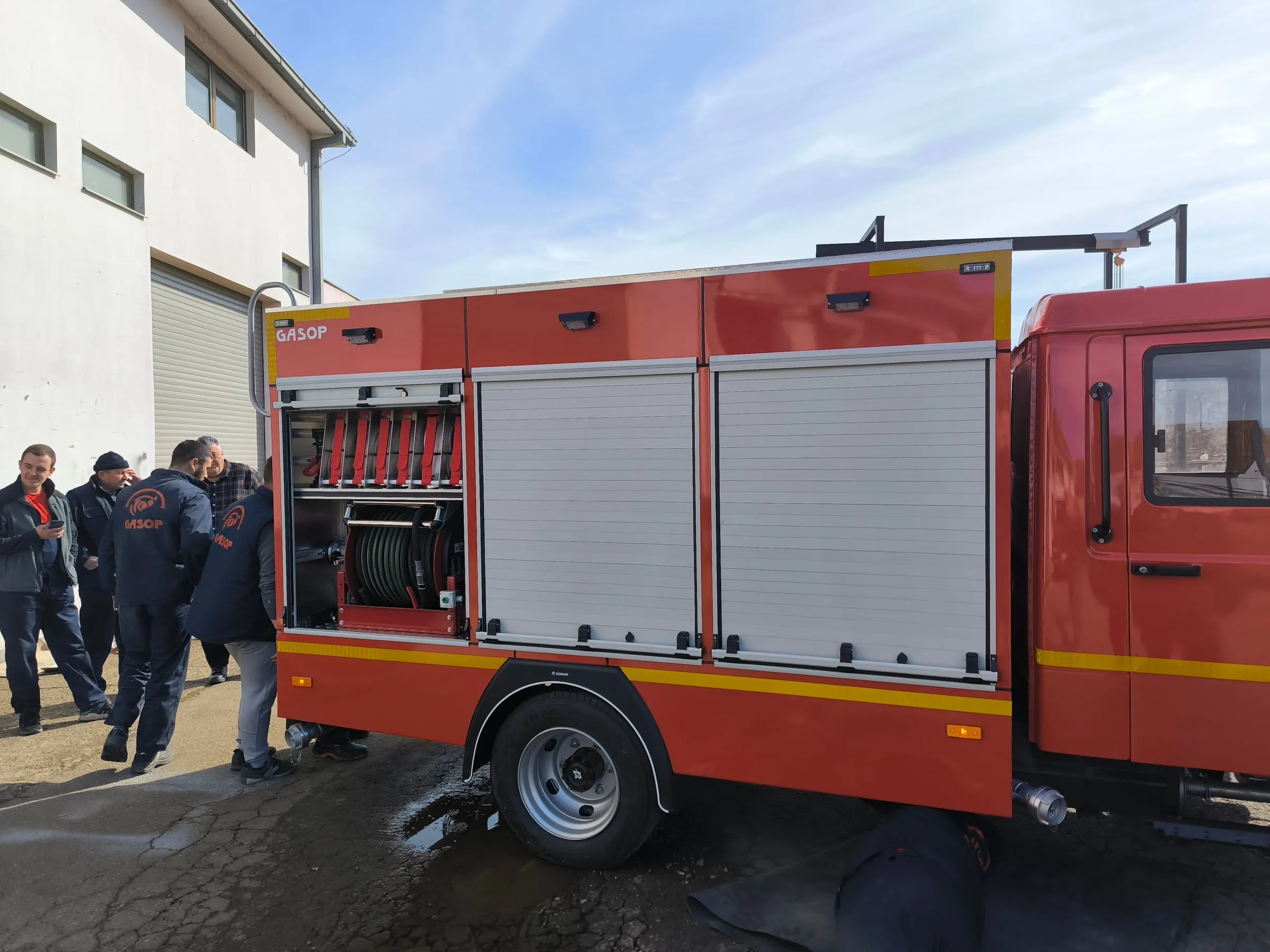 People beside an open firefighting vehicle compartment outside the workshop